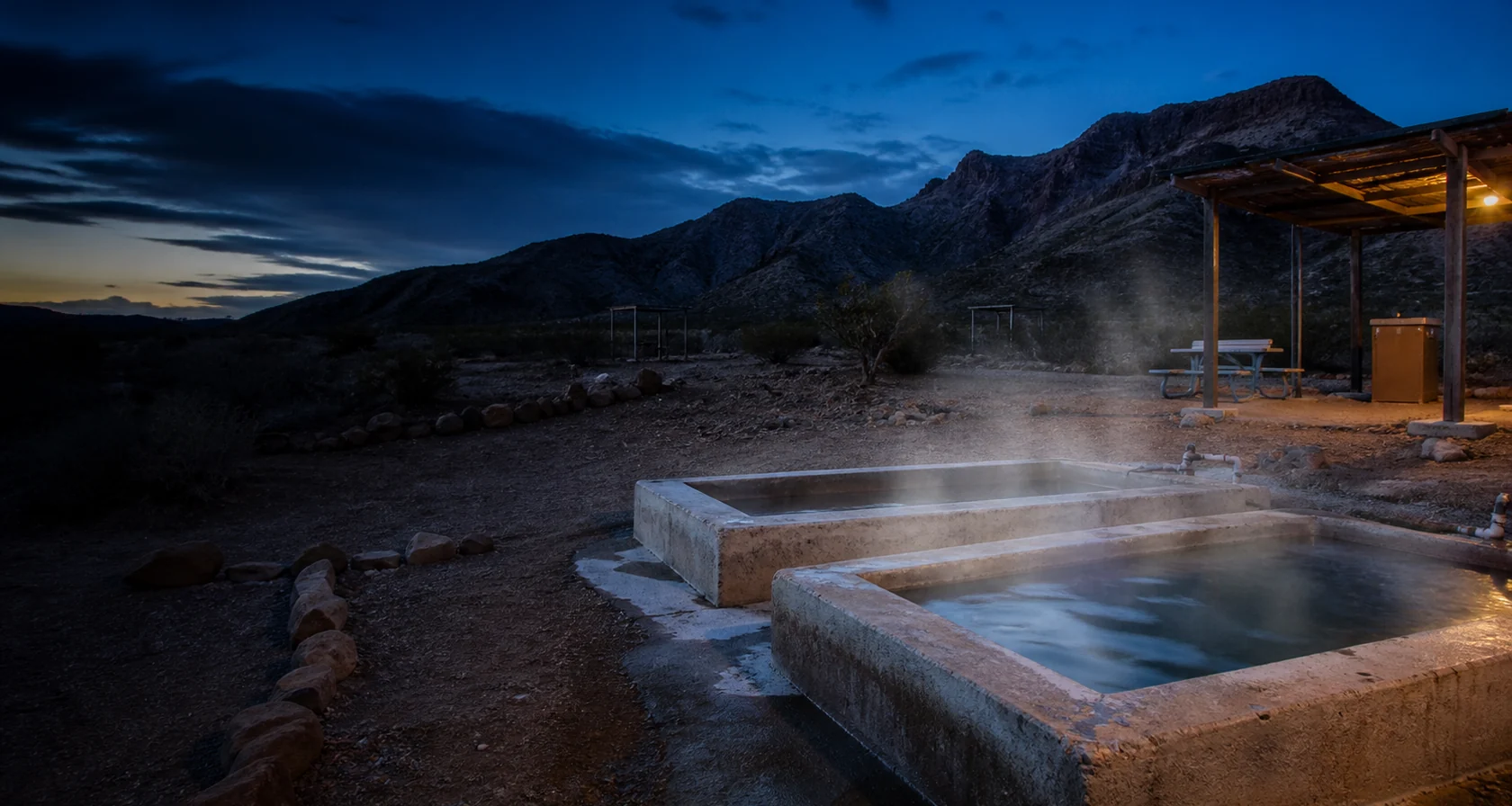 Two modest public soaking tubs in the primitive Hot Well desert setting at blue hour